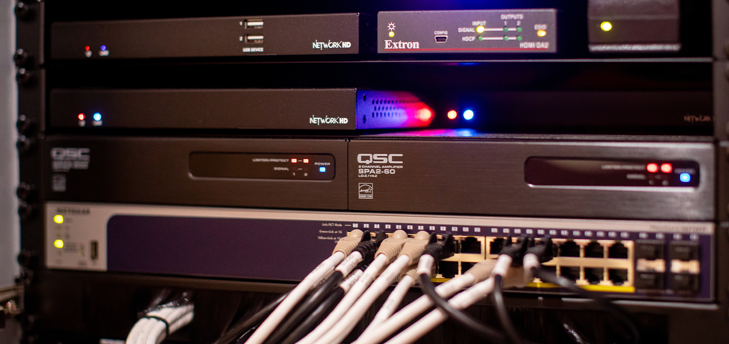 A rack filled with various computer equipment and numerous tangled wires, showcasing a complex setup.