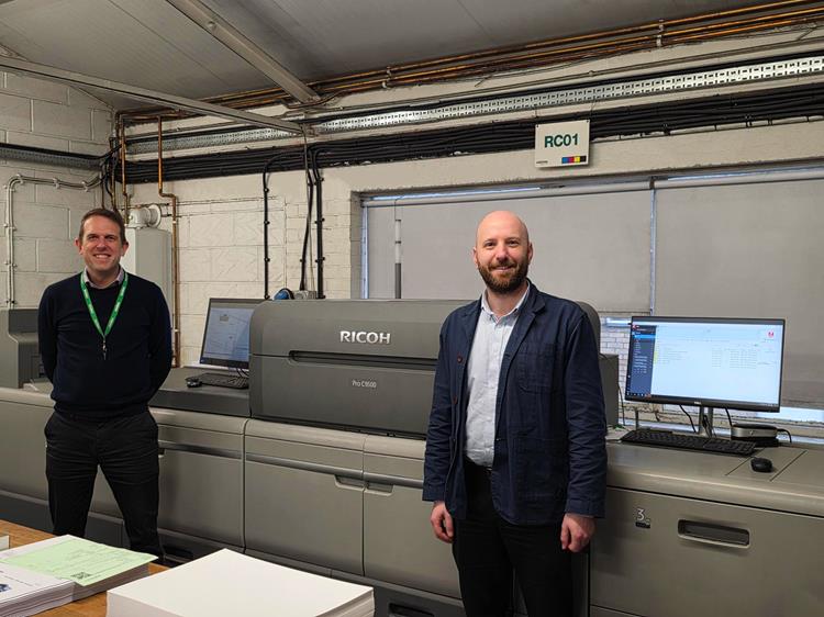 Two men standing in a room with a large printer