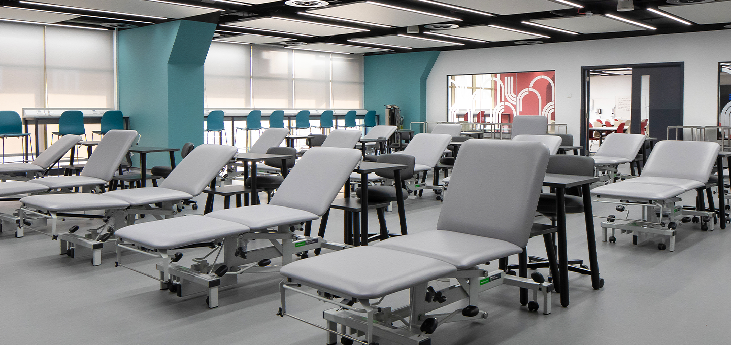 Modern clinical teaching lab with multiple adjustable treatment couches, tables and seating in a bright open space.