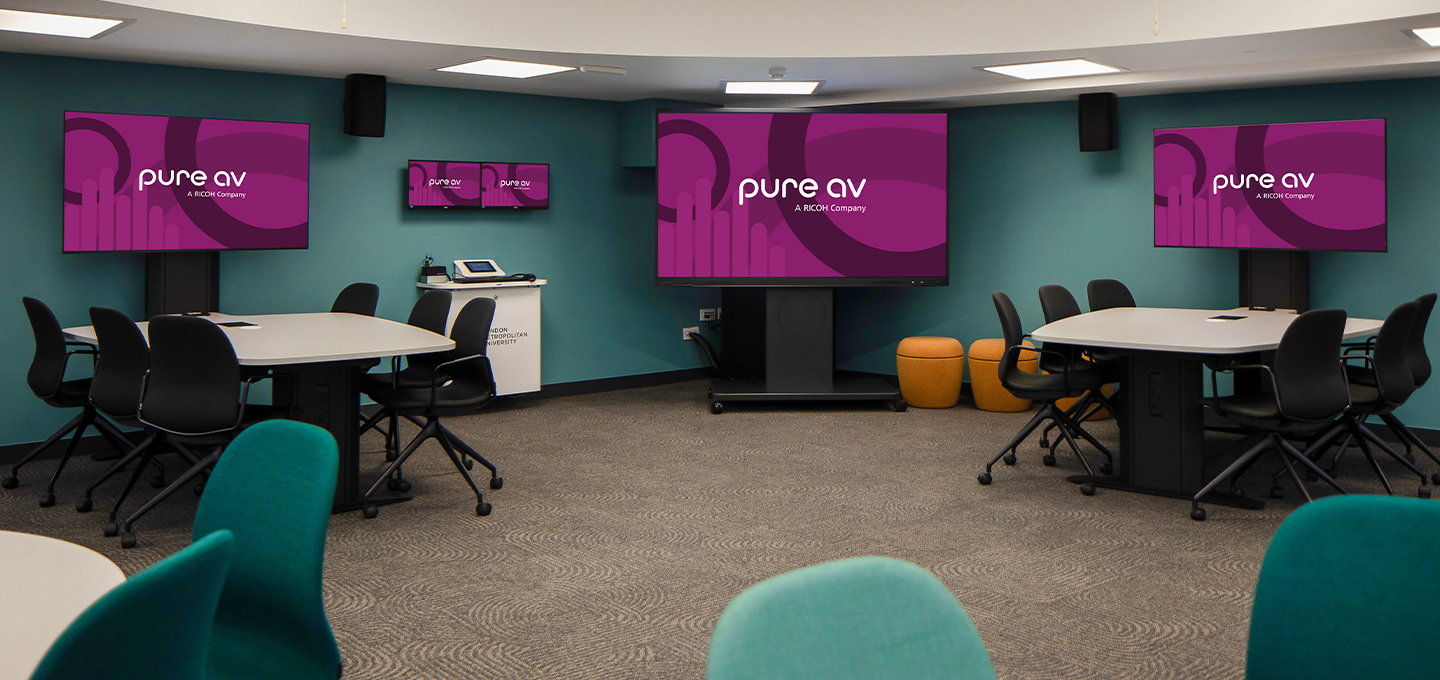 Modern collaborative learning space with round tables, chairs and multiple large interactive displays.