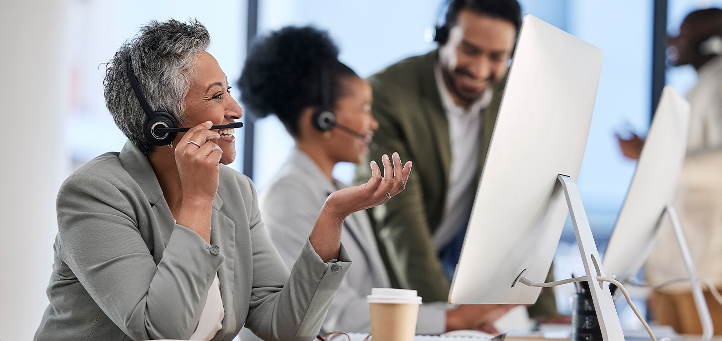 A smiling call center team works at computers with headsets, conveying teamwork and professionalism. A coffee cup is on the desk, adding a casual touch.